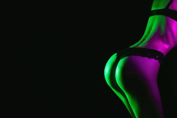 Sexy ass of woman in panties with drops of water and sweat on her body. Slim beautiful female body in underwear with neon light - Photo, image