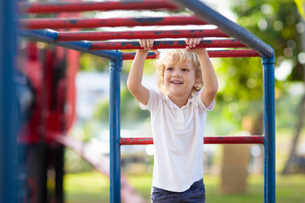 Child playing on outdoor playground in rain. Kids play on school or kindergarten yard. Active kid on colorful monkey bars. Healthy summer activity for children. Little boy climbing. - Foto, Imagen
