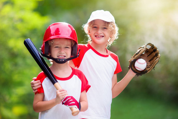 子供は野球をする。バットとボールを持つ子供。健康な子供のための屋外活動。男の子と女の子のための楽しいチームボールゲーム。野球界の若手選手。安全な運動のためのヘルメットを持つ小さな男の子. - 写真・画像