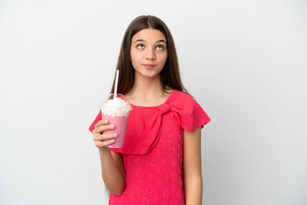 Little girl with strawberry milkshake over isolated white background and looking up - Фото, изображение