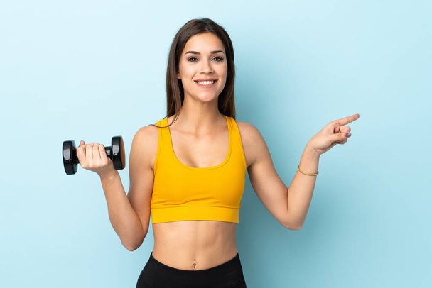Young caucasian woman making weightlifting isolated on blue background surprised and pointing finger to the side - Photo, Image