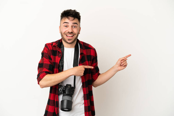 Молодой фотограф кавказский мужчина на белом фоне удивлен и указывает на сторону - Фото, изображение