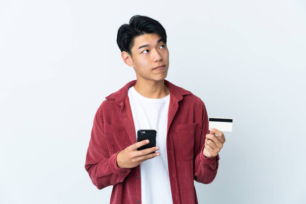 若いです中国人男孤立しましたホワイト背景購入とともにAモバイルとクレジットカードしばらく考えます - 写真・画像