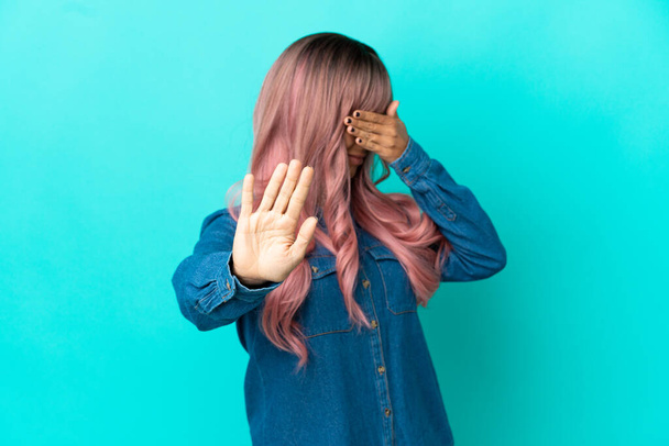 Młoda mieszanka rasy kobieta z różowymi włosami odizolowane na niebieskim tle co stop gest i pokrycie twarzy - Zdjęcie, obraz