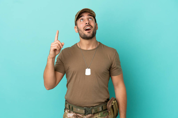 Military with dog tag over isolated on blue background pointing up and surprised - Photo, Image
