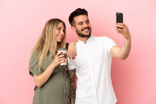 Kobieta w ciąży i mężczyzna na odizolowanym różowym tle robi selfie z telefonu komórkowego - Zdjęcie, obraz