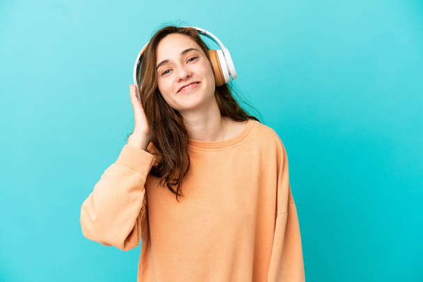 Young caucasian woman isolated on blue background listening music - Foto, afbeelding