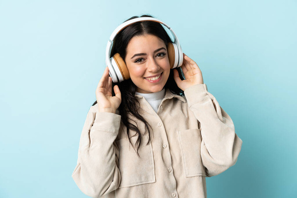 Молодая белая женщина, изолированная на синем фоне, слушает музыку - Фото, изображение