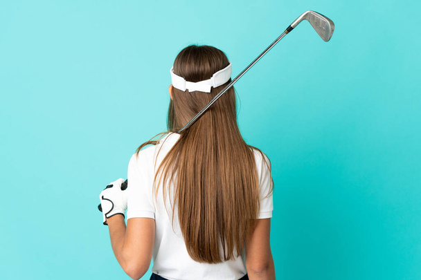 Молодая женщина на изолированном синем фоне играет в гольф и в задней позиции - Фото, изображение