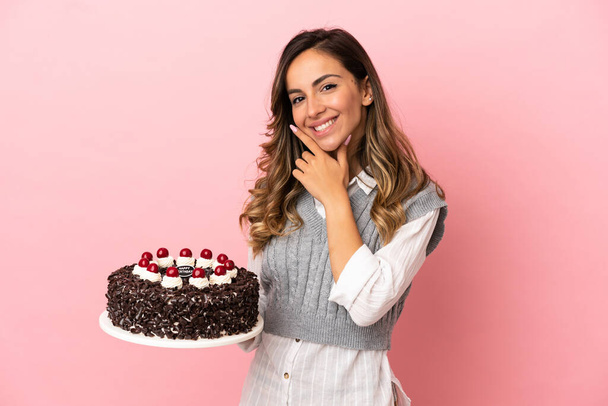 Mladá žena drží narozeninový dort přes izolované růžové pozadí šťastný a usmívající se - Fotografie, Obrázek