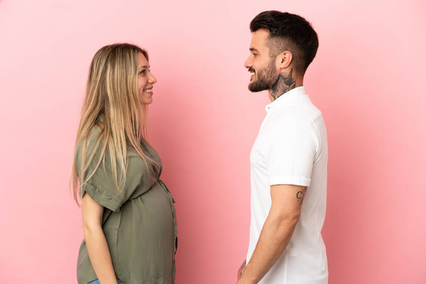 Pregnant woman and man over isolated pink background looking at each other - Fotografie, Obrázek