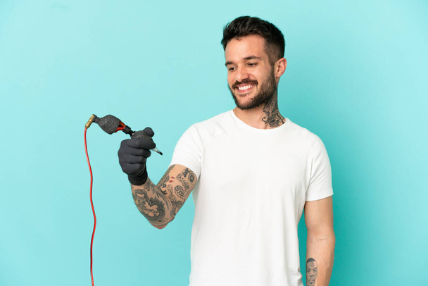Tattoo kunstenaar man over geïsoleerde blauwe achtergrond met gelukkige uitdrukking - Foto, afbeelding