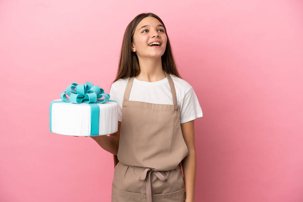 Little girl with a big cake over isolated pink background laughing - Foto, afbeelding