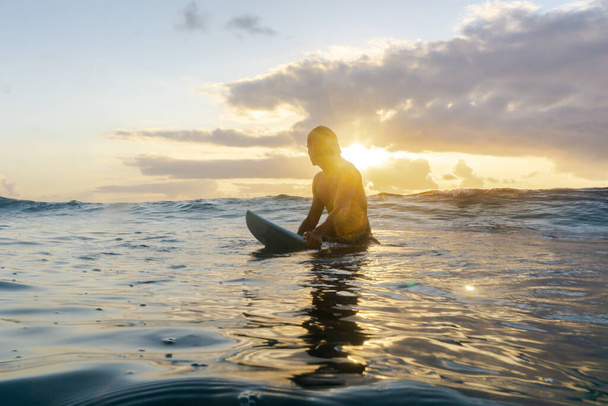 若い白人男性が早起きして日の出にサーフィンをする - 写真・画像