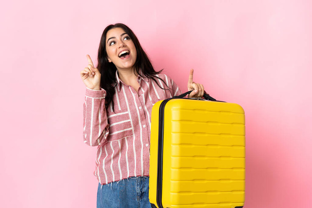 Молодая белая женщина изолирована на розовом фоне в отпуске с чемоданом путешествия и указывая вверх - Фото, изображение