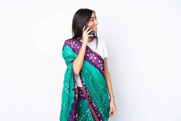 Молодая индийская женщина изолированы на белом фоне ведения разговора с мобильным телефоном с кем-то - Фото, изображение