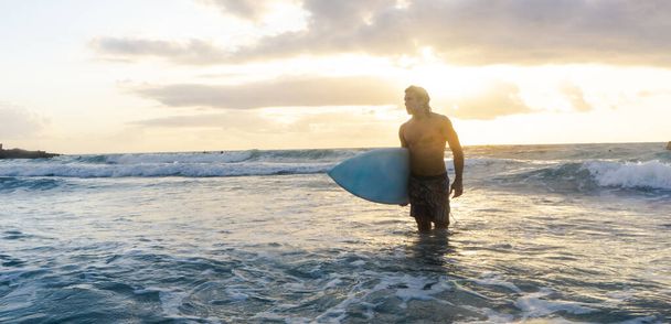 Nuori valkoihoinen mies nousee aikaisin surffaamaan auringonnousun aikaan. - Valokuva, kuva