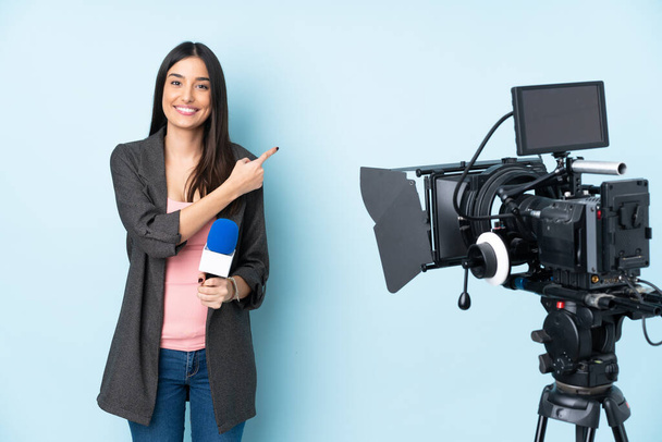Репортер жінка тримає мікрофон і звітує новини ізольовані на синьому фоні, вказуючи на бік, щоб представити продукт
 - Фото, зображення