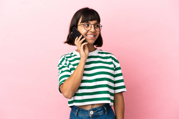Junge Frau mit gemischter Rasse isoliert auf rosa Hintergrund hält ein Gespräch mit dem Mobiltelefon - Foto, Bild