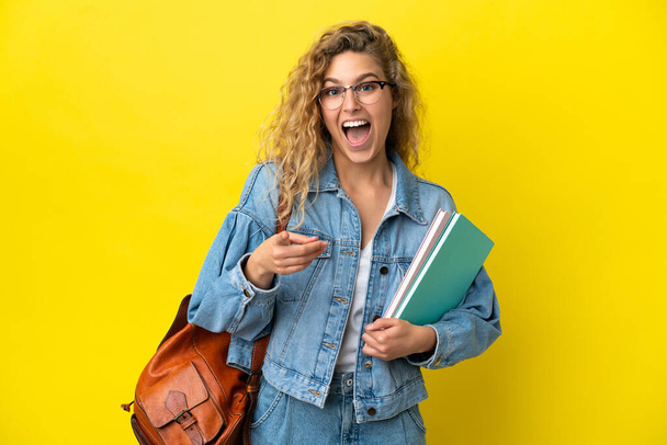 Young student caucasian woman isolated on yellow background surprised and pointing front - Photo, Image