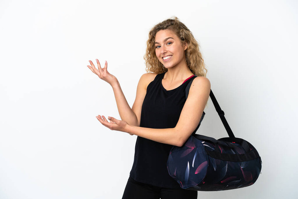 Young sport woman with sport bag isolated on white background extending hands to the side for inviting to come - Foto, Bild