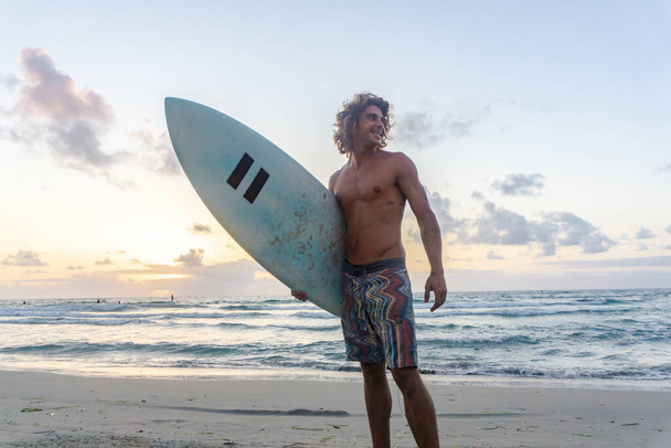 Młody biały mężczyzna wstaje wcześnie do surfowania o wschodzie słońca - Zdjęcie, obraz