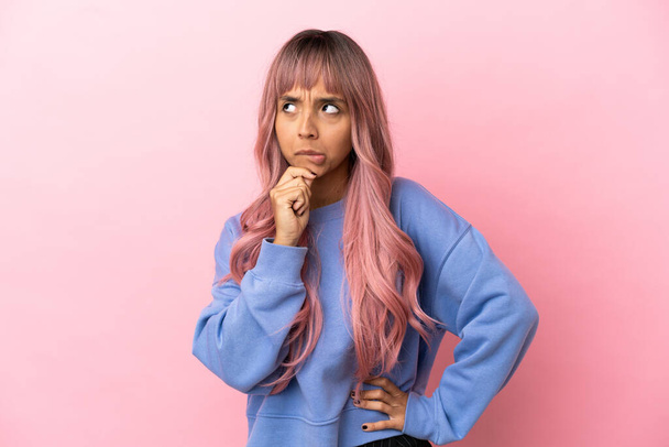 Mladá smíšená rasa žena s růžovými vlasy izolované na růžovém pozadí s pochybnostmi a myšlení - Fotografie, Obrázek