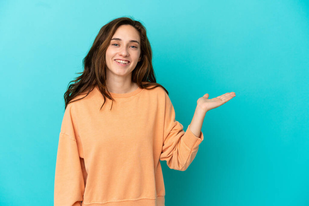 Young caucasian woman isolated on blue background holding copyspace imaginary on the palm to insert an ad - Photo, Image