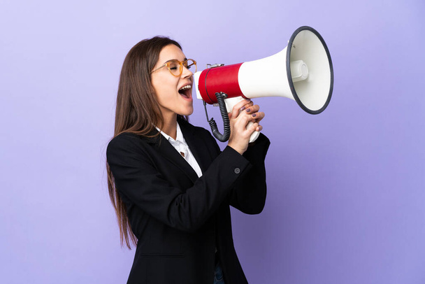 Business woman isolated on purple background shouting through a megaphone - Foto, imagen