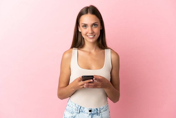 Jonge vrouw over geïsoleerde roze achtergrond verzenden van een bericht met de mobiele - Foto, afbeelding