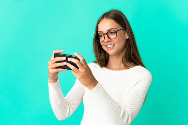 Молода жінка над ізольованим синім тлом, граючи з мобільним телефоном
 - Фото, зображення
