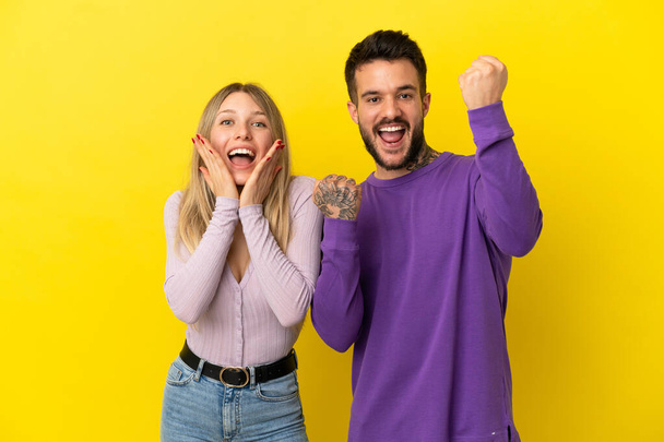 Young couple over isolated yellow background celebrating a victory - Foto, Imagen