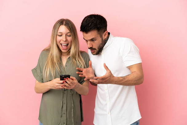 Беременная женщина и мужчина на изолированном розовом фоне отправлять сообщение или письмо с мобильного телефона - Фото, изображение