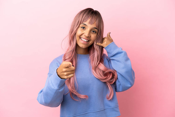 Молодая женщина смешанной расы с розовыми волосами изолированы на розовом фоне делает телефон жест и указывая вперед - Фото, изображение