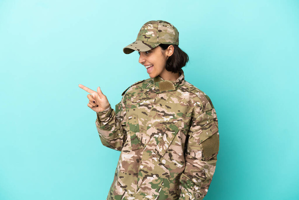 Militar mulher de raça mista isolado no fundo azul apontando o dedo para o lado e apresentando um produto - Foto, Imagem