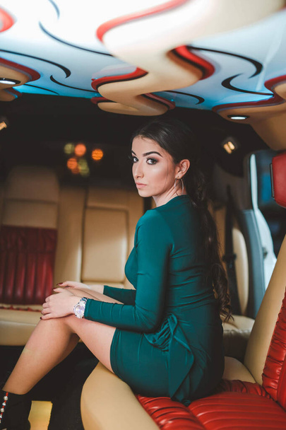 A shallow focus of a brunette woman wearing a green dress and sitting in a luxurious limousine - Fotografie, Obrázek
