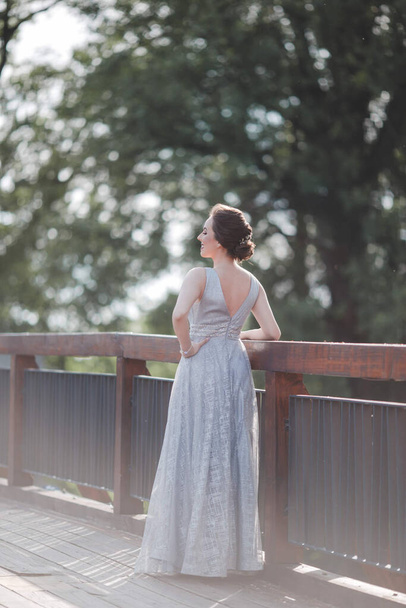 A portrait of a brunette Caucasian woman wearing a long gray dress and leaning on fences in a park - Foto, immagini