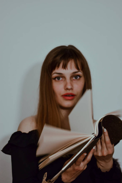 A vertical portrait of a young caucasian female holding an open notebook with a surprised face - Photo, Image