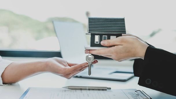 Übergeben Sie einem Immobilienmakler das Hausmodell und erklären Sie der Käuferin den Geschäftsvertrag, die Miete, den Kauf, die Hypothek, den Kredit oder die Hausversicherung.. - Foto, Bild