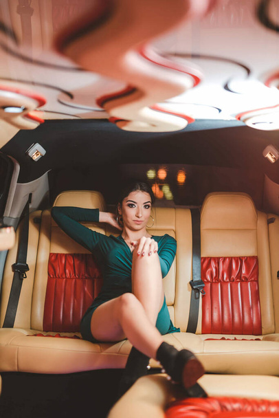 An adult brunette woman wearing a green dress and sitting in a luxurious limousine - Φωτογραφία, εικόνα