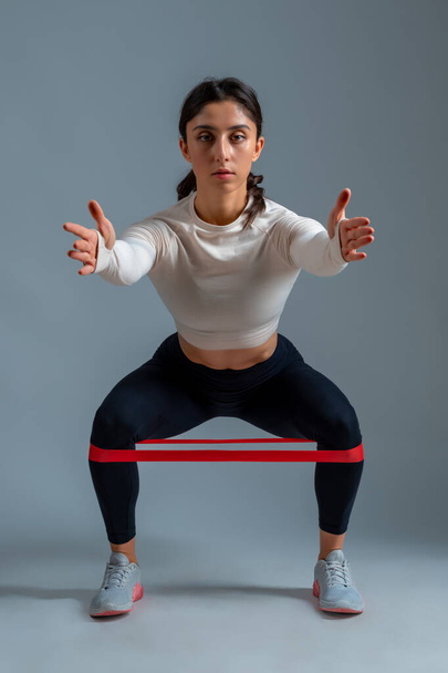 Girl doing squats with resistance band on grey background - Fotografie, Obrázek