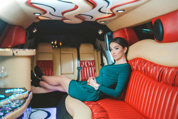 An adult brunette woman wearing a green dress and sitting in a luxurious limousine - Fotoğraf, Görsel