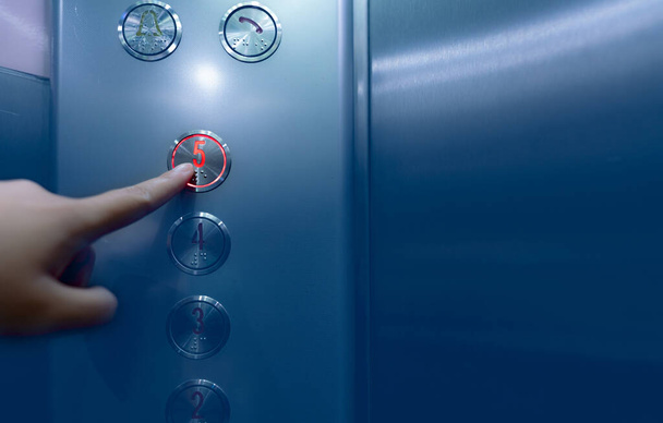 Egy személy nyomja meg a lift gomb ötödik emeletét. Kézzel nyomja meg az 5-ös gombot az irodai vagy szállodai liftben. Indexujj nyomja meg a lift gombot. Klausztrofóbia. Az emberek beragadtak a liftbe. Braille-kód. - Fotó, kép