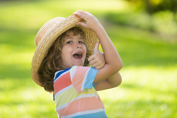 Portrait of a happy laughing child in summer nature park with thumbs up sign. Positive kids in straw hat. Summer vacation. - 写真・画像