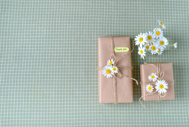 Caixa de presente envolto com papel artesanal marrom e decorado com flores de camomila naturais com palavras de gratidão. Vista superior, flat lay, lugar para texto. Foto de alta qualidade - Foto, Imagem