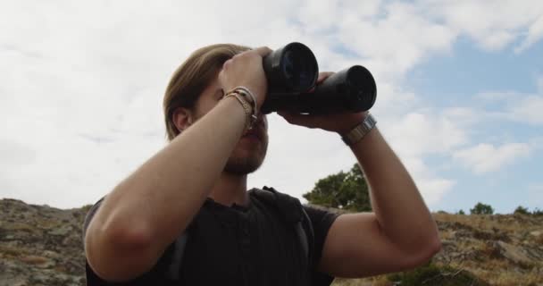 Młody człowiek spoglądający w lornetkę na zielone góry w dzień   - Materiał filmowy, wideo