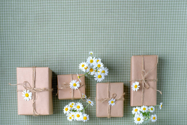 Zestaw pudełek zapakowanych w brązowy papier rzemieślniczy i ozdobionych naturalnymi kwiatami rumianku. Widok z góry, płaski, miejsce na tekst. Wysokiej jakości zdjęcie - Zdjęcie, obraz