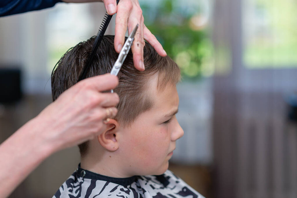 Um menino bonito recebendo corte de cabelo por cabeleireiro na barbearia. Vista lateral.Close-up. - Foto, Imagem