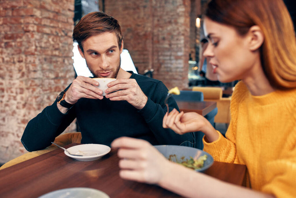 žena večeří u stolu v kavárně a muž s šálkem kávy v pozadí - Fotografie, Obrázek