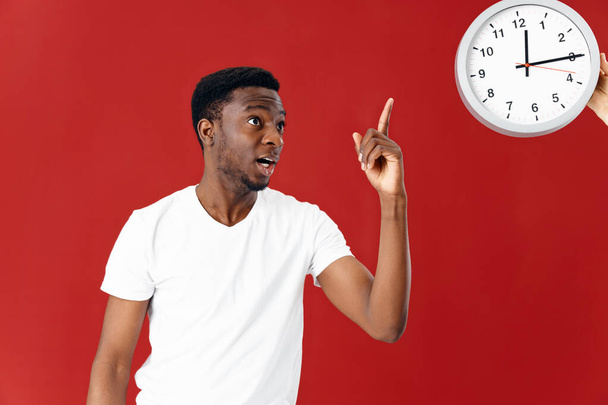 emotional man in white t-shirt shows on watch red background - 写真・画像